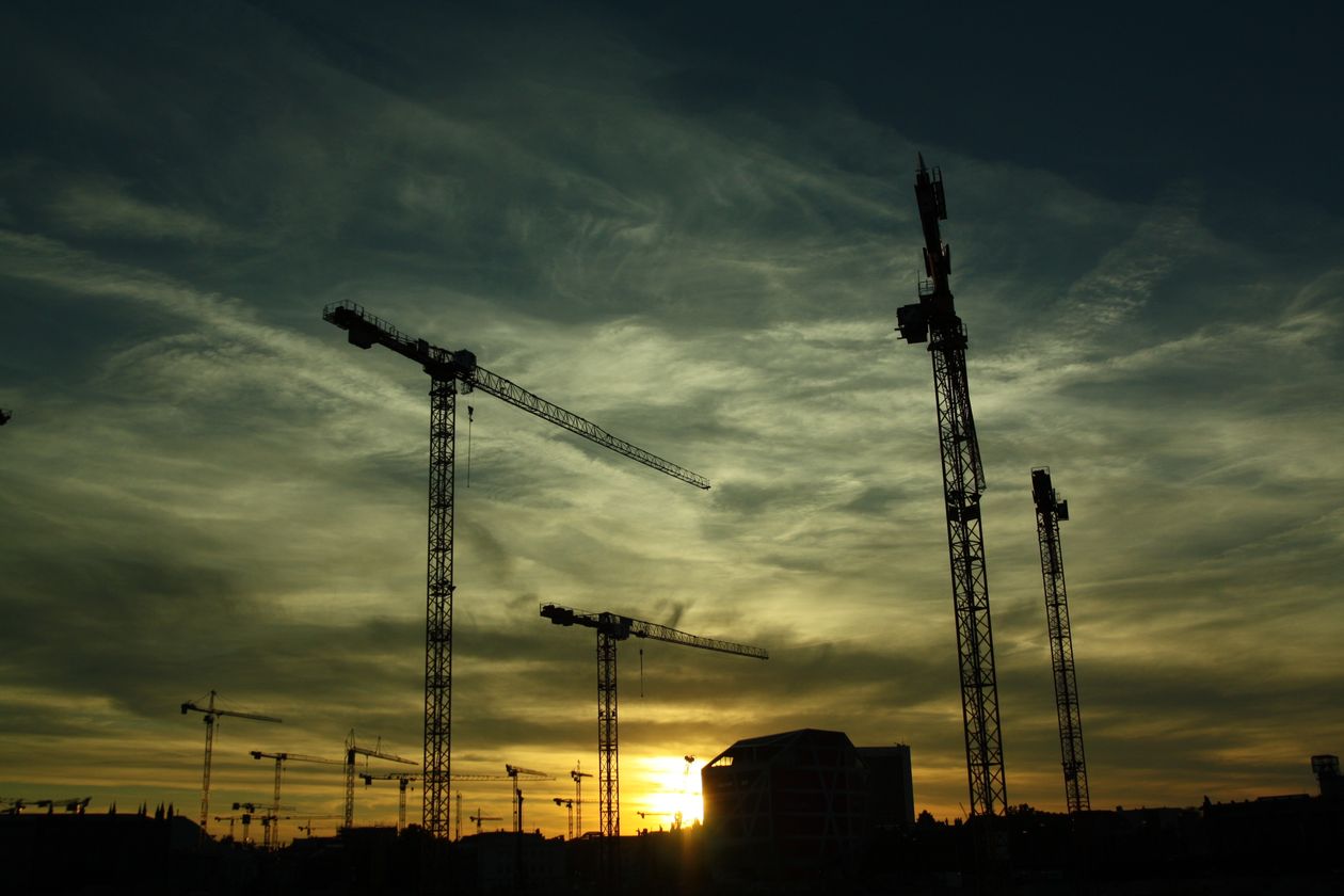 Silhouette of construction cranes at a work site during sunset