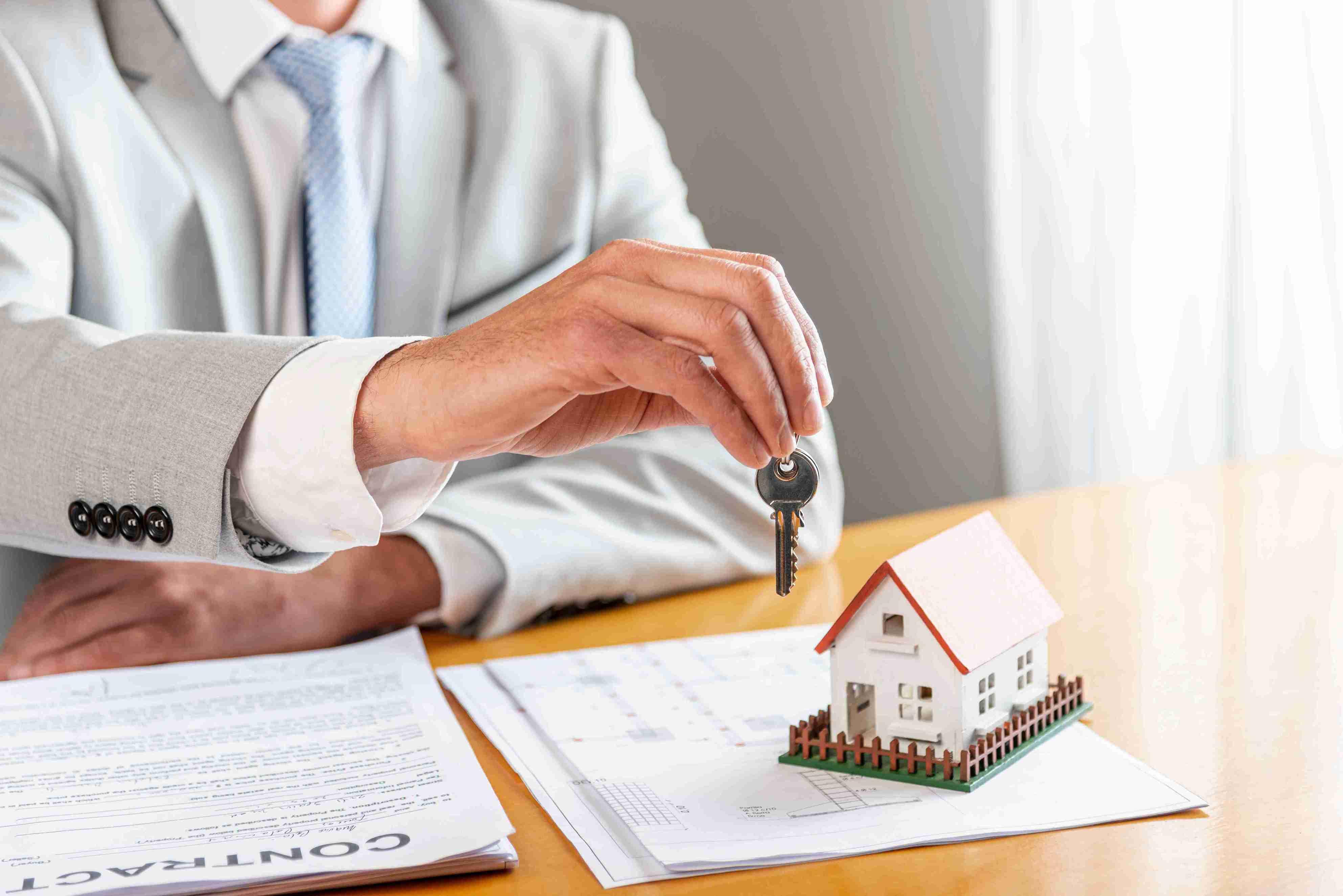 person-holding-house-keys-toy-model-house-desk (1)_11zon