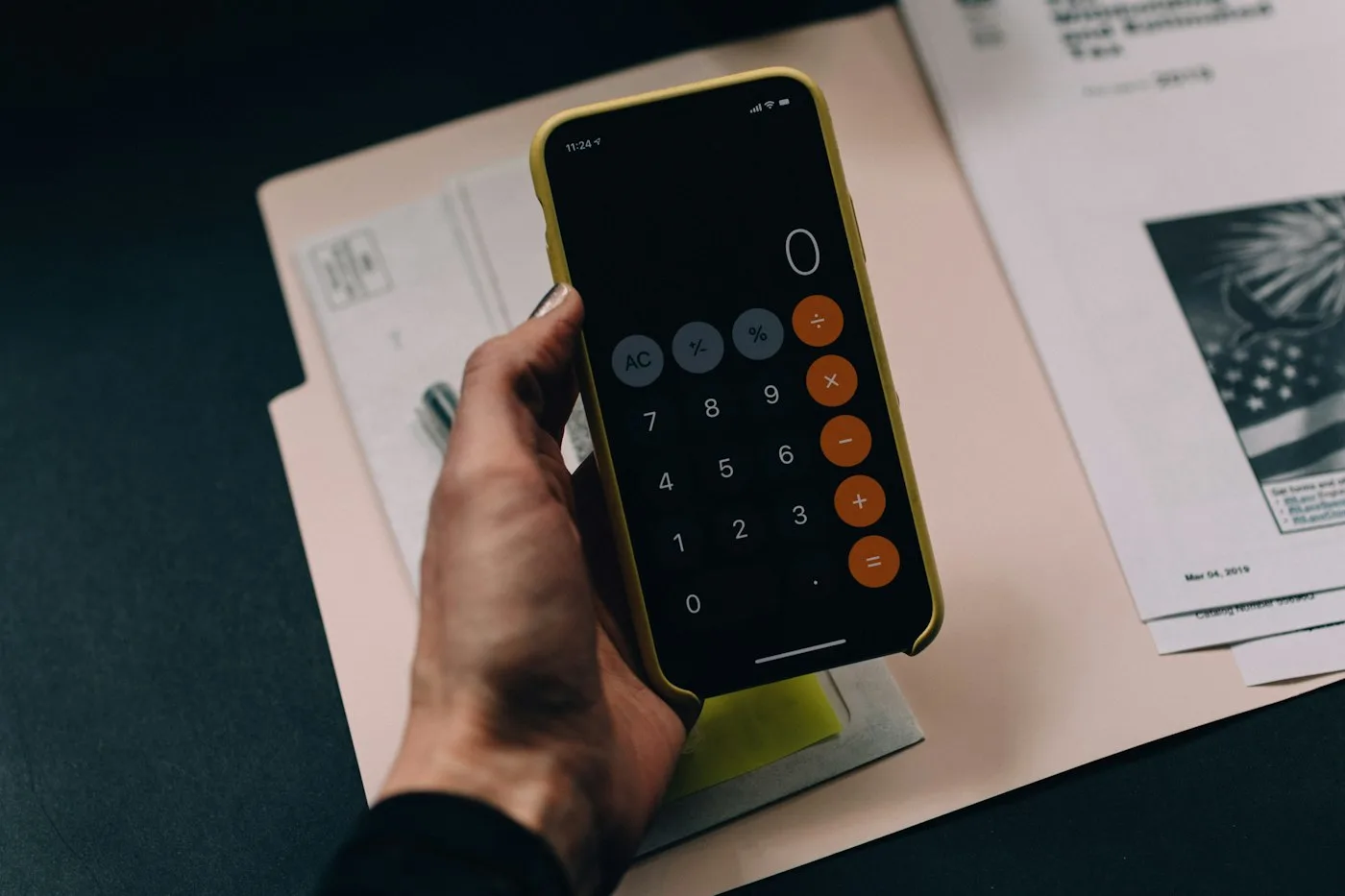 Hand holding a smartphone showing a calculator app over a paper folder